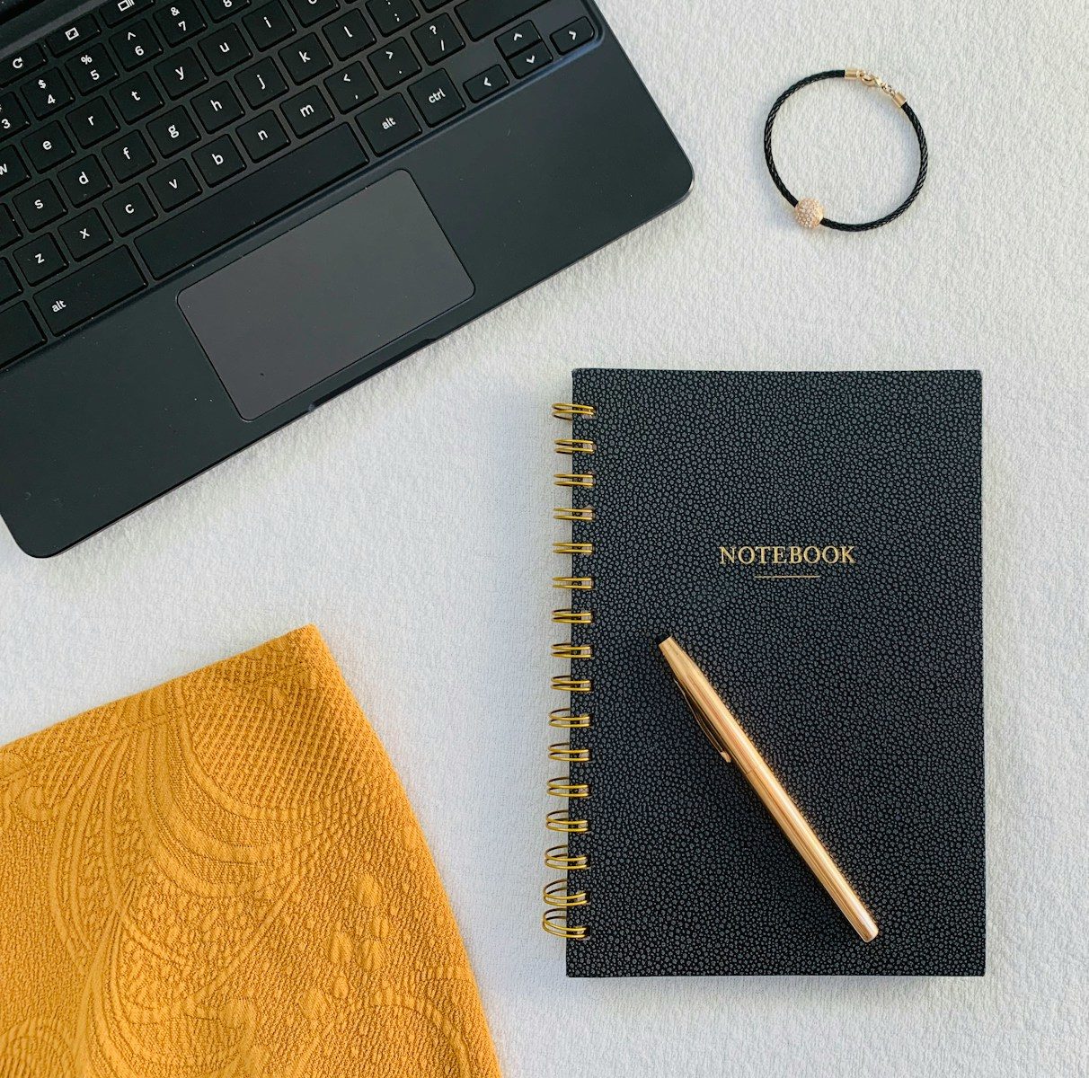 flatlay photo of black spiral notebook, gold retractable pen, and space gray MacBook